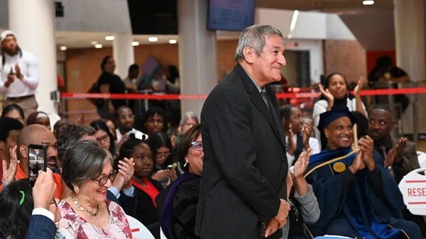 Mario A Acosta stands smiling at a gathering, surrounded by attendees, including Derrick Tremaine Brazill, in a large indoor space.